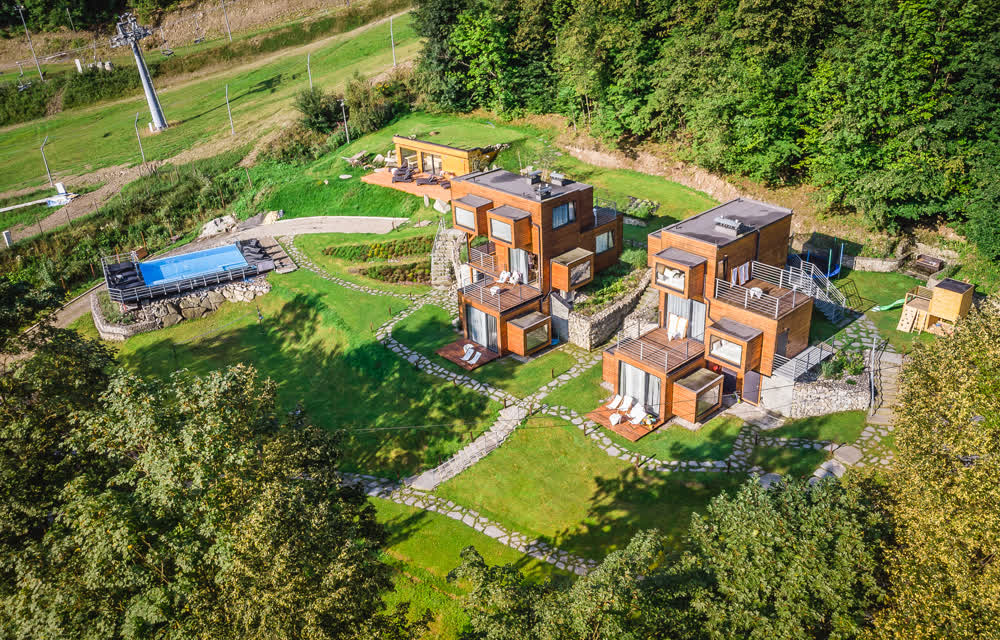 Apartamenty Szuflandia w Wiśle z lotu ptaka wiosną — domki, basen i zielone wzgórza
